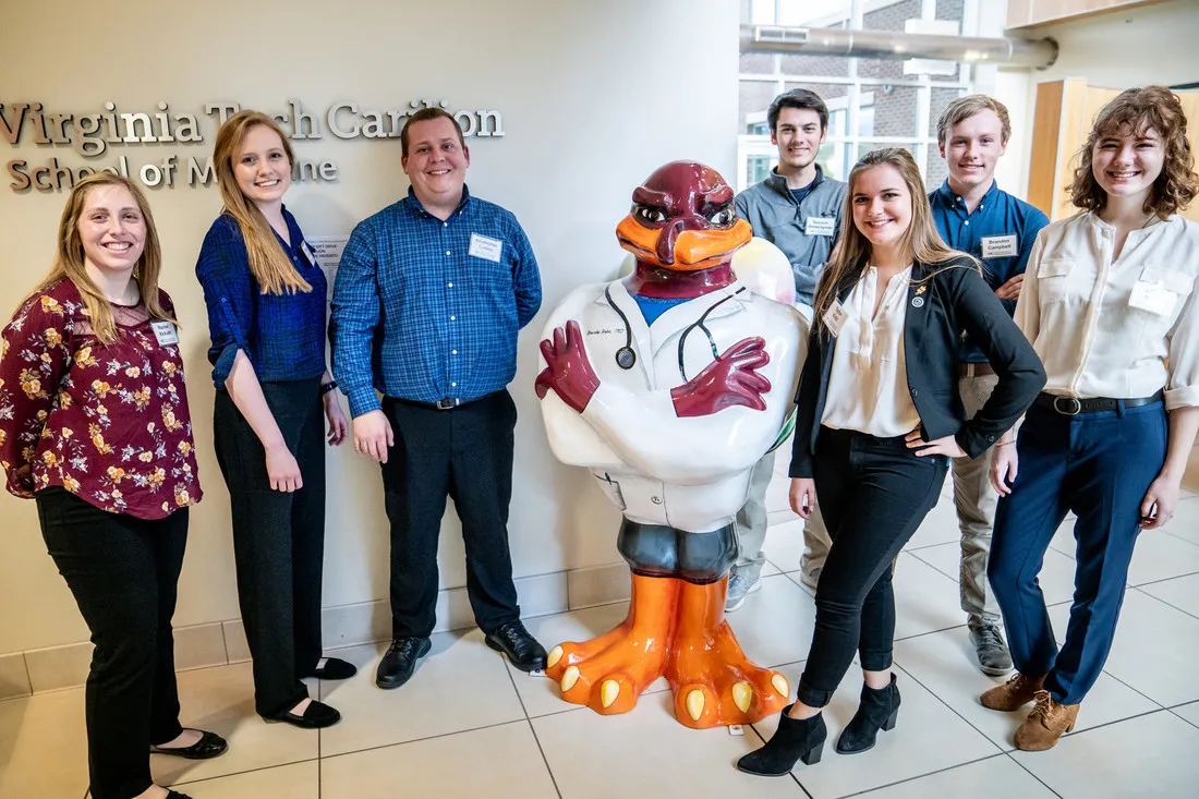 Group of men and women around the VT Hokie Bird with a lab coat on